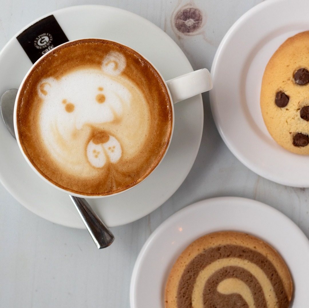 Café latte con un osito dibujado en la espuma, junto a galletas de chispas y de espiral