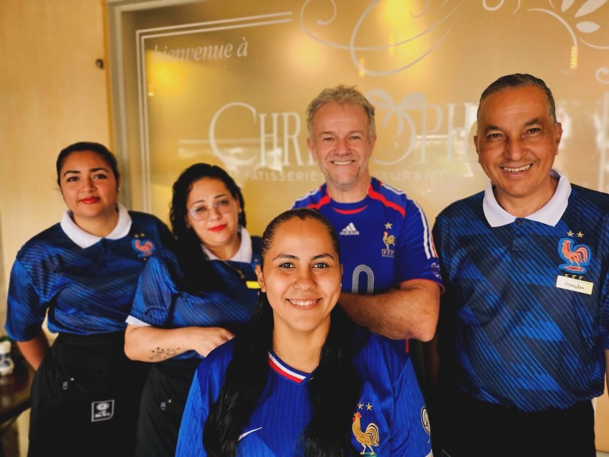 Cinco integrantes del equipo sonriendo con camisetas de Francia frente al vidrio grabado de la entrada