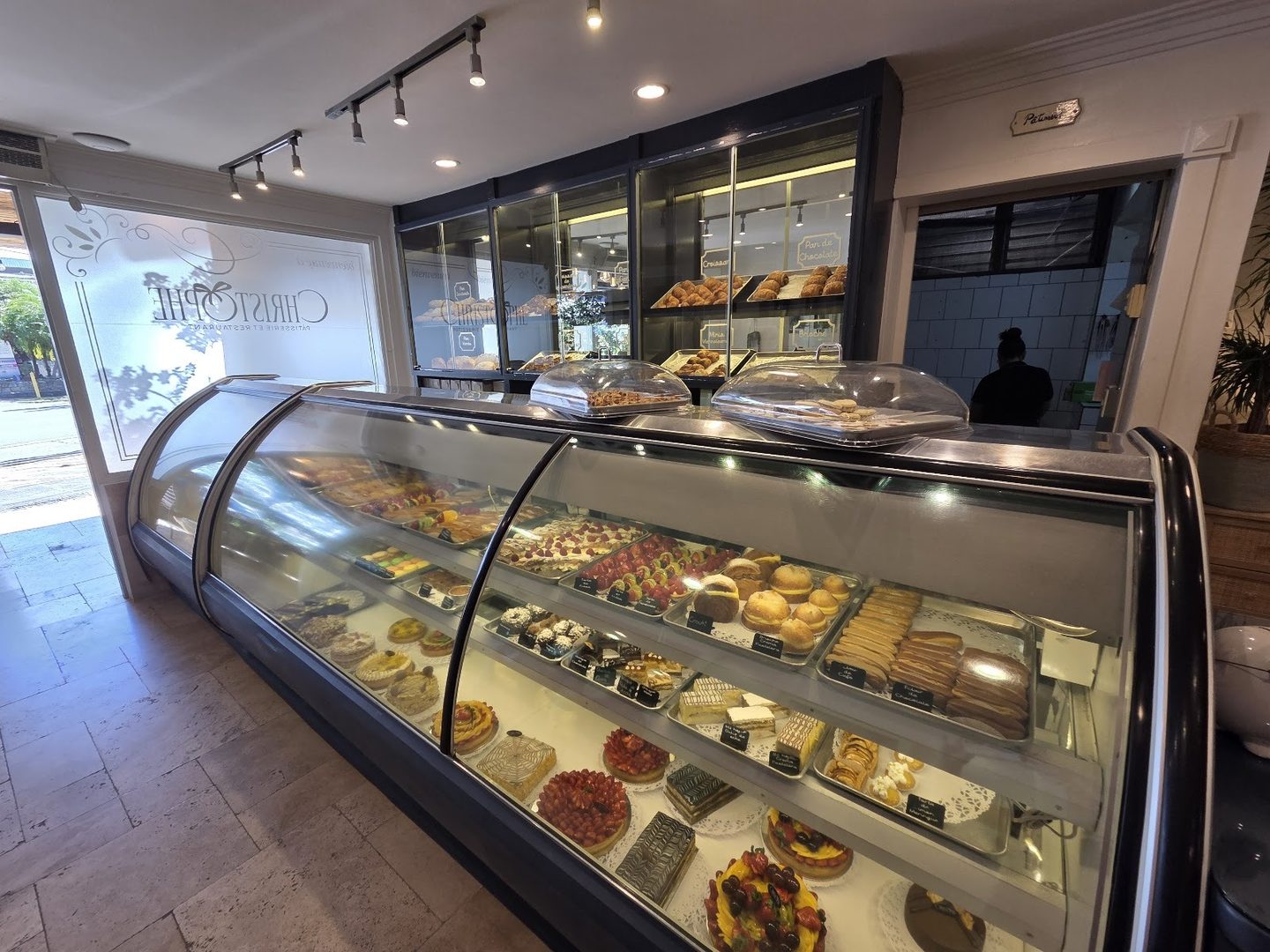 La vitrina de pastelería de Chez Christophe llena de tartas y éclairs, con el nombre grabado en el vidrio de la entrada