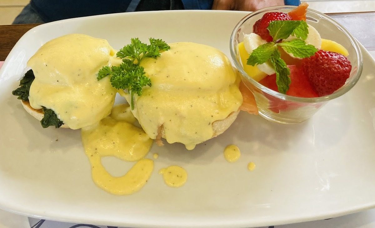 Plato de huevos benedictinos con salsa holandesa y un vaso de frutas frescas