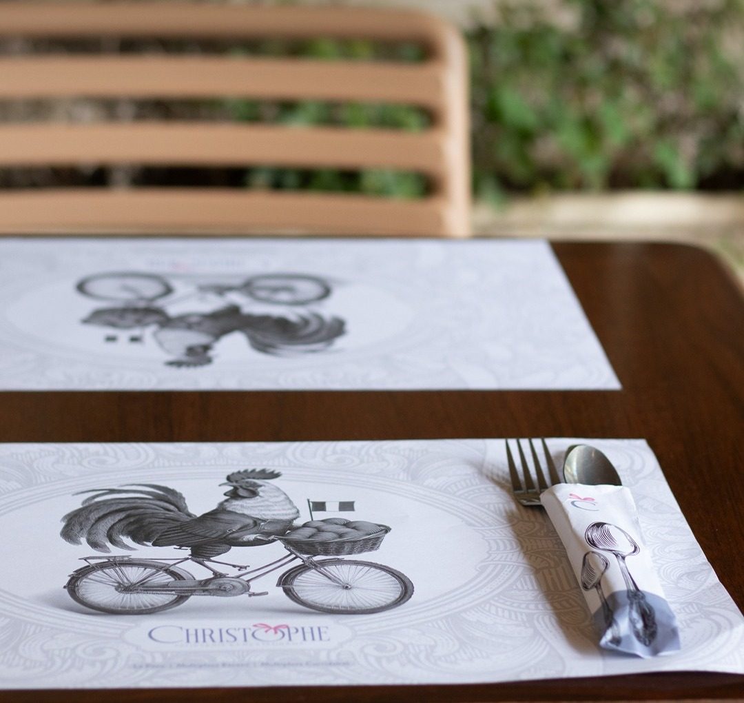 Manteles individuales de papel con un gallo en bicicleta y cubiertos envueltos sobre la mesa