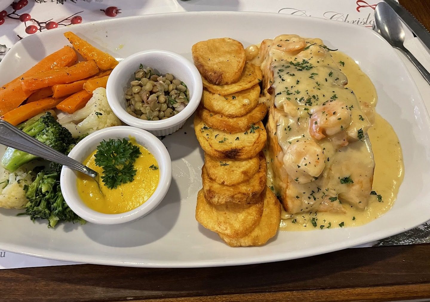 Salmón con salsa de camarón, papas redondas y vegetales servido sobre el mantel de la casa